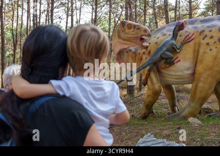 Una donna e un bambino osservano una scena realistica di attacco di dinosauri nel parco a tema dei dinosauri Dino Parque a Lourinhã, Portogallo. Europa Foto Stock