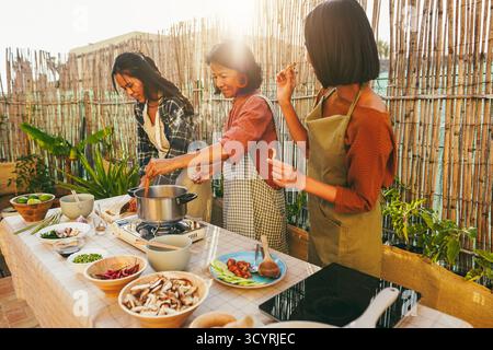 Famiglia asiatica che cucinano cibo tailandese insieme nel patio all'aperto - madre e due figlie si divertono a preparare l'insalata di papaya Foto Stock