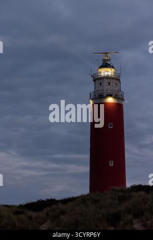 Eierland, De Cocksdorp, Texel, Paesi Bassi, Oktober 28th, 2024, Un maestoso faro rosso si erge orgogliosamente illuminato contro un cielo lunare, guidando le navi al sicuro a casa Foto Stock