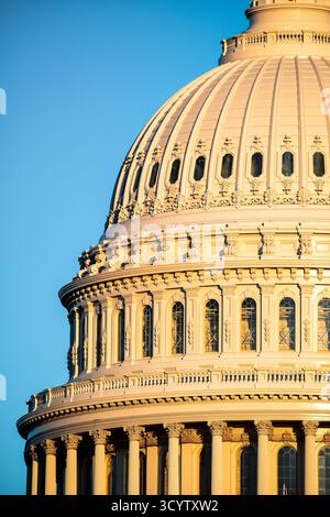 Cupola del Campidoglio americano illuminata dal sole dorato Washington DC | WASHINGTON D.C., Stati Uniti — La luce del tramonto riscalda i cornicioni a gradini e le finestre ad arco della cupola del Campidoglio americano, vista dal basso contro un cielo sereno. La cupola in ghisa, progettata da Thomas U. Walter, fu costruita in fasi dal 1855 al 1866 e rimane il punto centrale architettonico del complesso del Campidoglio su Capitol Hill. Foto Stock