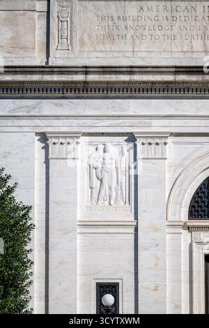 American Institute of Pharmacy Building Bas Relief Washington DC // WASHINGTON DC — Un importante pannello a bassorilievo raffigurante "PHARMAKEVTIKE" (farmacia), scolpito da Lee Lawrie, si trova sulla facciata principale dell'American Institute of Pharmacy Building. Questo rilievo in marmo bianco è uno dei numerosi elementi artistici che adornano la struttura neoclassica. Progettato dall'architetto John Russell Pope e completato nel 1934, l'edificio funge da quartier generale nazionale dell'American Pharmacists Association (APHA). La sua iscrizione sottolinea la sua dedizione al progresso della farmacia, della salute pubblica Foto Stock