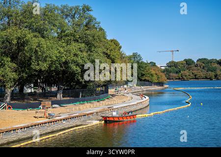 Tidal Basin Seawall Construction Project Washington DC // WASHINGTON DC — i progressi nel Tidal Basin Seawall Construction Project si vedono il 17 ottobre 2025, guardando da Inlet Bridge verso il National Mall. Questo progetto di infrastrutture critiche affronta il problema del cedimento e dell'innalzamento del livello del mare, che incide sullo storico bacino delle maree. Il Franklin Delano Roosevelt (FDR) Memorial è visibile dietro gli alberi sulla sinistra. I lavori in corso mirano a proteggere i monumenti iconici e i famosi ciliegi che circondano il bacino. I lavoratori edili e le attrezzature sono visibili lungo il lungomare appena rinforzato. Foto Stock