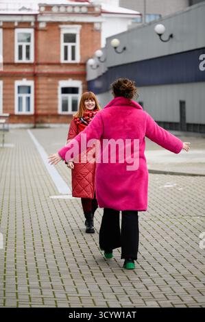 Le donne camminano l'una verso l'altra, le braccia si spalancano, abbracciando calorosamente. Gli amici si scambiano abbracci gioiosi in ambienti urbani, incontrandosi all'aria aperta come amici in c Foto Stock