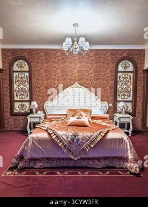 Grand hotel suite con una camera da letto riccamente decorata con un letto grande e confortevole, comodino antico e intricati motivi murali, perfetta per un Foto Stock
