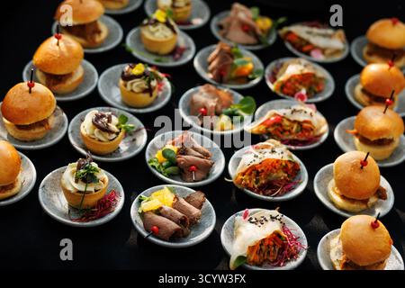 Vari mini bocconcini tra cui panini, fette di manzo, involtini di verdure e tartine disposti su piccoli piatti. Ideale per catering, eventi o ricevimenti. Foto Stock