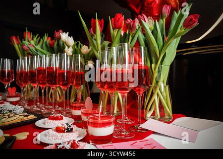 Cocktail rossi in bicchieri da champagne con tulipani e dolci dessert su un tavolo di San Valentino decorato. Ideale per feste romantiche e a tema Foto Stock