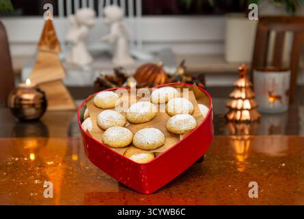 Su un tavolo decorato a Natale c'è una scatola di biscotti a forma di cuore con biscotti rotondi alla vaniglia spolverati con zucchero a velo. Sullo sfondo due angeli di gesso Foto Stock