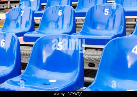 Lo stadio è in plastica blu brillante con 5, 6 e 7 posti a sedere in tribuna vuota, creando un'atmosfera tranquilla e ordinata, perfetta per lo sport, vigilia Foto Stock