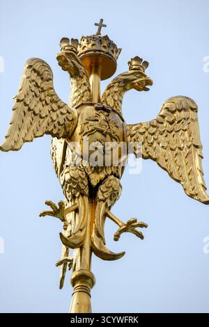 Una statua dorata a due teste di aquila coronata e arroccata in cima a un palo. Questo emblema imperiale russo evoca sovranità, arte araldica e senza tempo Foto Stock