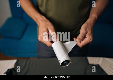 Primo piano di un uomo che stacca lo strato usato di rullo di lanugine appiccicoso, preparandosi a pulire i vestiti da polvere, capelli e fibre, assicurandosi di indossare gli indumenti Foto Stock