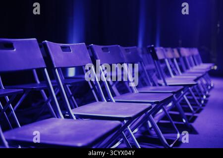 File di sedie vuote preparate per i partecipanti alla presentazione in una sala conferenze. Illuminato da luce blu. Pianificazione degli eventi. Foto Stock