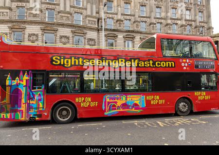Autobus turistico rosso con grafica colorata parcheggiato in una strada della città di fronte all'architettura storica di Belfast nell'Irlanda del Nord Foto Stock