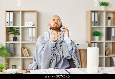 Giovane malato affetto da mal di gola seduto sul posto di lavoro in ufficio e che parla al telefono cellulare. Foto Stock