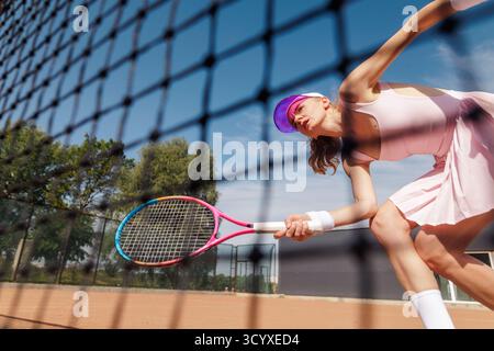 Vista dinamica ad angolo basso della donna atleta di tennis che gioca a rally in rete con azione incentrata sulla racchetta ed energia sul campo in terra battuta Foto Stock
