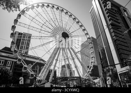 La ruota panoramica SkyView Atlanta sorge sopra le strade del centro, incorniciata da moderni grattacieli e storici edifici in mattoni rossi in bianco e nero Foto Stock