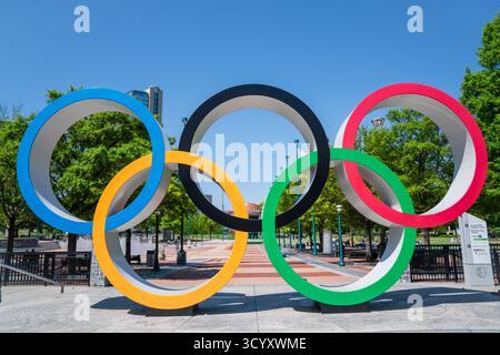 Il colorato monumento degli anelli Olimpici si erge in modo prominente nel Centennial Olympic Park, circondato da alberi e passerelle sotto un cielo primaverile azzurro Foto Stock