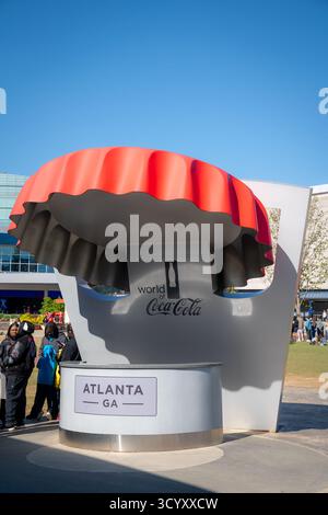 I visitatori si fermano vicino alla grande scultura di berretto rosso all'ingresso del World of Coca-Cola in una mattinata luminosa e soleggiata nel centro di Atlanta Foto Stock