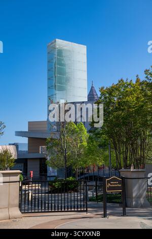 La torre di vetro della Coca-Cola sorge sopra il World of Coca-Cola a Pemberton Place, incorniciata da alberi e da un cielo azzurro cristallino nel centro di Atlanta Foto Stock