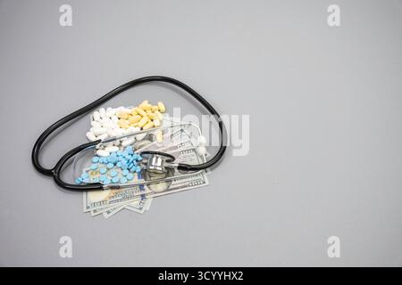 Uno stetoscopio e tre diverse pillole da prescrizione sopra una pila di banconote da 100 dollari. Foto Stock
