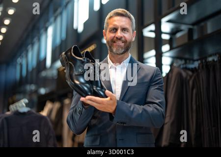 Un uomo elegante in costume ammira le scarpe di lusso in una boutique. Un uomo d'affari sceglie con fiducia calzature eleganti in un negozio di scarpe. Scarpe classiche in pelle Foto Stock