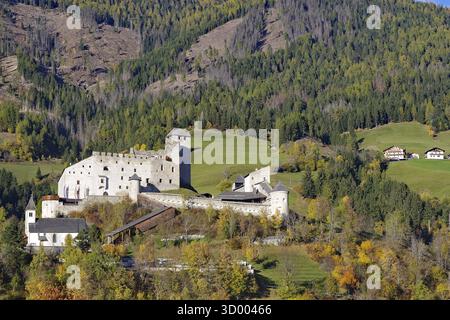 Castello medievale su boschi autunnali e prati in un paesaggio montano soleggiato, Herbstenburg, pista ciclabile del Drau, Toblach, Tirolo, Austria Foto Stock