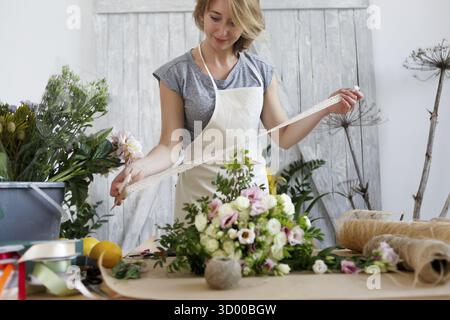 Fioraio con bel bouquet e nastro in mani al negozio di fiori Foto Stock