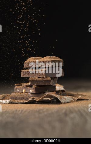 Rotto il cioccolato poroso e con i dadi sul tavolo di legno, sfondo nero Foto Stock