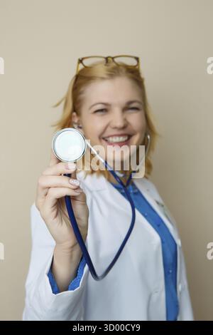Bella bionda con fonendoscopio in abito medicale su sfondo vuoto Foto Stock