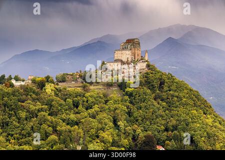 Un pittoresco sentiero di montagna si snoda attraverso il verde lussureggiante delle Alpi piemontesi, con vista sull'imponente Sacra di San Michele, che si erge sul mare Foto Stock