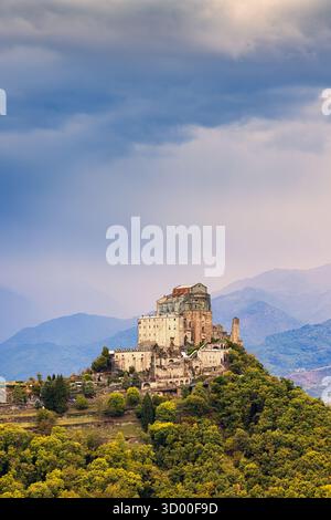 Un pittoresco sentiero di montagna si snoda attraverso il verde lussureggiante delle Alpi piemontesi, con vista sull'imponente Sacra di San Michele, che si erge sul mare Foto Stock