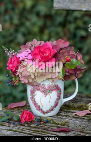 bouquet di rose rosa e ortensie fiorisce in una tazza con ornamento cardiaco Foto Stock