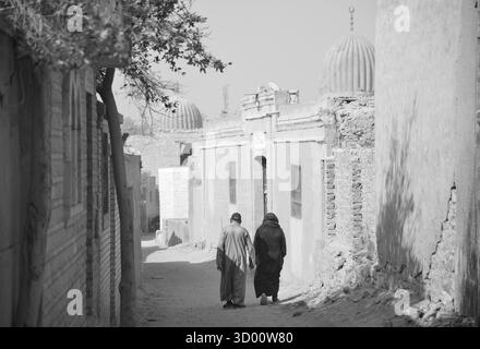 Due persone camminano lungo una strada stretta e polverosa fiancheggiata da vecchi edifici nella città dei morti, il Cairo, in Egitto. Foto Stock