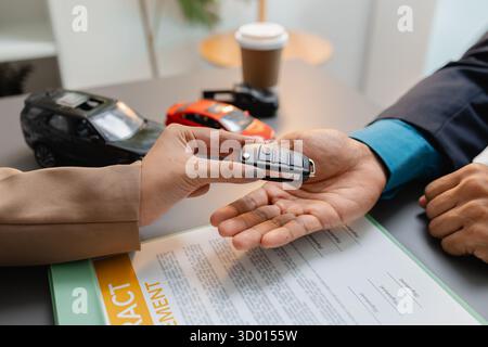 Un uomo d'affari e un cliente stanno esaminando e firmando un contratto di vendita di auto presso una scrivania, con modellini di auto di piccole dimensioni, una tazza di caffè e documenti intorno a loro, Foto Stock