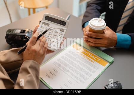Un uomo d'affari e un cliente stanno esaminando e firmando un contratto di vendita di auto presso una scrivania, con modellini di auto di piccole dimensioni, una tazza di caffè e documenti intorno a loro, Foto Stock