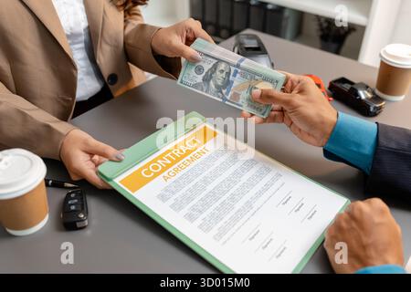 Un uomo d'affari e un cliente stanno esaminando e firmando un contratto di vendita di auto presso una scrivania, con modellini di auto di piccole dimensioni, una tazza di caffè e documenti intorno a loro, Foto Stock