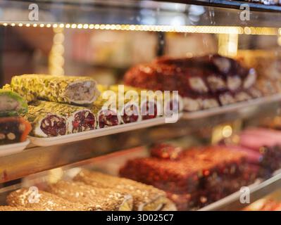 Ripiani pieni di una serie di dolci tradizionali, caratterizzati da colori e texture vivaci. L'esposizione include dessert arrotolati adornati con noci e. Foto Stock
