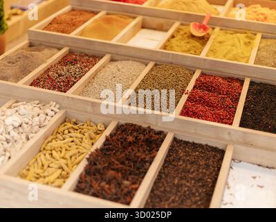 Una vivace selezione di spezie è organizzata in vassoi di legno in un mercato. Ogni vassoio può contenere condimenti diversi, mostrando vari colori e texture Foto Stock