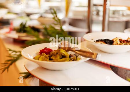 Una selezione di stuzzichini colorati è esposta in ciotole bianche su un tavolo a buffet. L'ambiente è luminoso e invitante, perfetto per un pranzo vivace Foto Stock