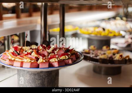 Un vibrante assortimento di dessert e' organizzato su un tavolo a buffet, caratterizzato da torte a strati e dolci colorati conditi con frutta fresca e panna, crea Foto Stock