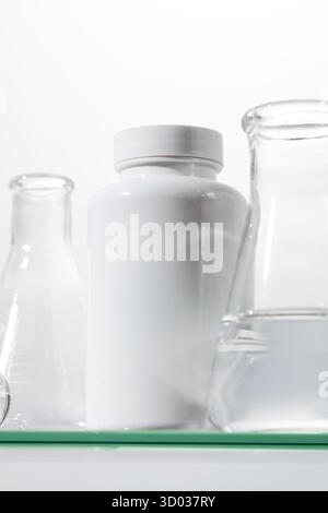 Un vaso bianco con vitamine o medicinali con utensili da laboratorio su un ripiano di vetro. Il concetto di medicinali, sostanze biologicamente attive. Foto Stock