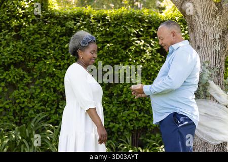 Coppia senior che si scambiano anelli in giardino, celebrando l'amore e l'impegno all'aperto. Matrimonio, matrimonio, romanticismo, anziani, cerimonia || modello rilasciato Foto Stock