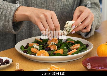 Donna che prepara l'insalata con insalata di spinaci freschi con arance, formaggio blu e noci pecan. Concetto di cibo sano Foto Stock