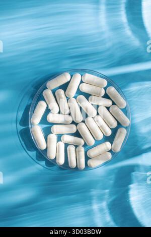 Capsule medicinali bianche, vitamine o integratori alimentari in primo piano su sfondo blu. Il concetto di medicina. Foto Stock