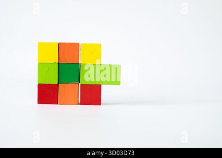 Blocchi di legno colorati disposti in uno stile geometrico creativo, formando una griglia con estensione verde orizzontale su sfondo bianco, a simboleggiare l'educa Foto Stock