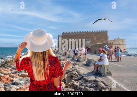 Vista della fortezza veneziana di Heraklion con Una donna bionda in un abito floreale rosso Foto Stock