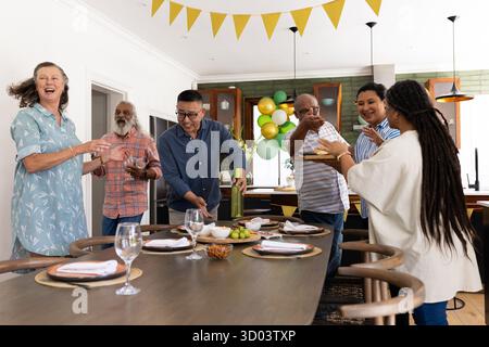 Un gruppo di anziani che festeggiano a casa, si divertono a ridere e conversare. Celebrazione, diversità, anziani, felicità, raccolta, community || modello rilasciato Foto Stock