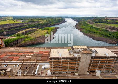 Itaipu Binacional, Brasile - 22 giugno 2025: La massiccia centrale elettrica della diga di Itaipu, con il fiume Parana che scorre attraverso il canale di scarico in cemento. Foto Stock
