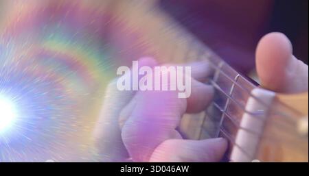 Premendo la mano sinistra del musicista che forma un accordo su corde di chitarra acustica in studio con un flare arcobaleno Foto Stock