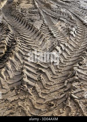 Vista ravvicinata dei cingoli dei pneumatici fangosi lasciati dai veicoli da cantiere pesanti in cantiere, formando schemi ripetitivi testurizzati nel terreno Foto Stock