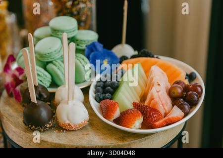 Piatto di frutta colorata con caramelle e macaron in una vivace esposizione di dessert in un locale luminoso Foto Stock